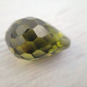 May include: A faceted green glass bead with a pear shape.