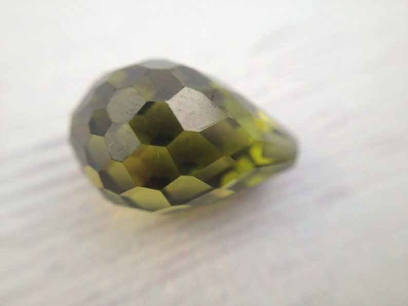 May include: A faceted green glass bead with a pear shape.
