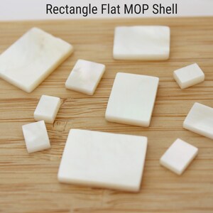 Puede incluir: Surtido de piezas de concha de nácar plana rectangular blanca de varios tamaños sobre una superficie de madera. Concha de nácar plana rectangular.