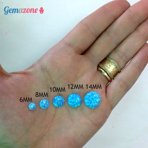 May include: A hand holding six blue opal cabochons in different sizes, ranging from 6mm to 14mm. The cabochons are arranged in a row from smallest to largest. The text "6MM", "8MM", "10MM", "12MM", and "14MM" is printed below the cabochons.