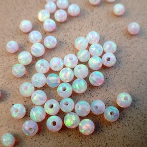 May include: A collection of white opal beads with iridescent rainbow colors. The beads are round and have a hole in the center for stringing.