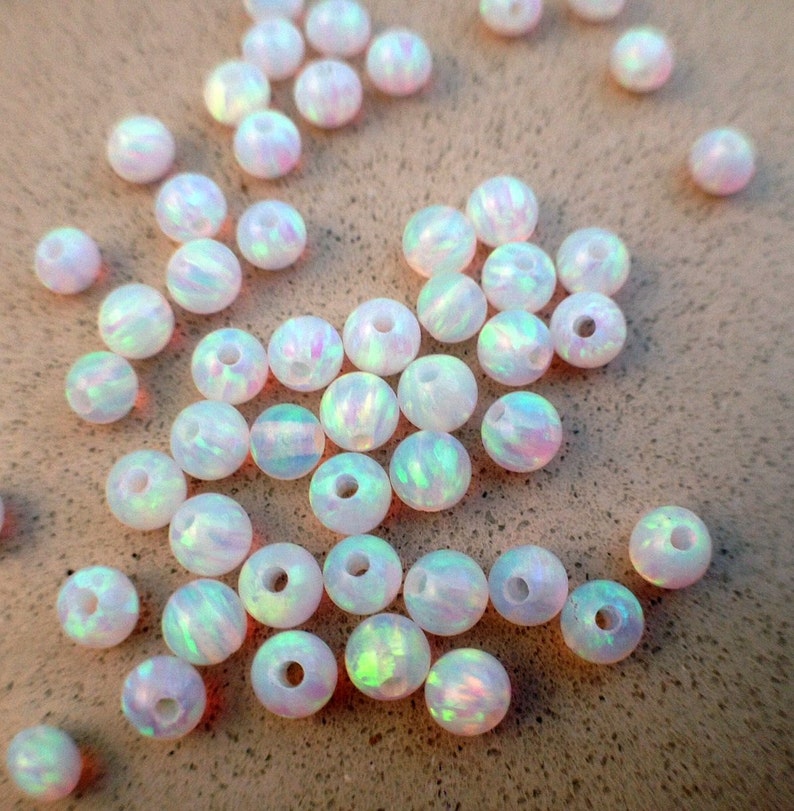 May include: A collection of white opal beads with iridescent rainbow colors. The beads are round and have a hole in the center for stringing.