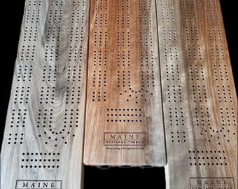 May include: Three wooden cribbage boards with a natural wood finish. Each board has a rectangular label with the text "MAINE HERITAGE TIMBER Recovering A Forgotten Forest".