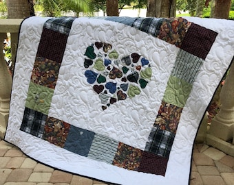 May include: A white quilt with a large heart made of smaller hearts in shades of blue, green, and brown. The quilt is made of patchwork fabric and has a white background with a quilted pattern.