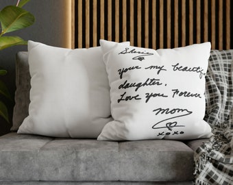 May include: Two white throw pillows with black handwritten text on one pillow. The text reads "Sharing your my beautiful daughter. Love you forever Mom xoxo". The pillows are on a gray couch with a black and white throw blanket.