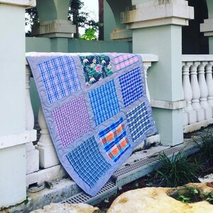 May include: A patchwork quilt made from different plaid fabrics in shades of blue, pink, and gray. The quilt is folded and draped over a railing.