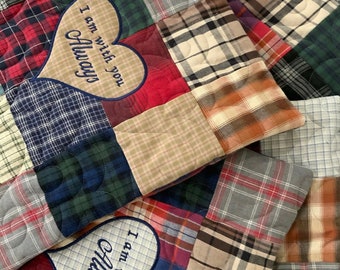 Può includere: Una trapunta patchwork con una toppa a forma di cuore che dice "Sono sempre con te". La trapunta è realizzata con diversi tessuti a quadri in tonalità di blu, verde, rosso e marrone.