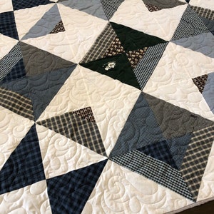 May include: A white quilt with a swirling pattern. The quilt is made of various shades of blue and brown plaid fabric. The quilt is made up of triangles and squares.