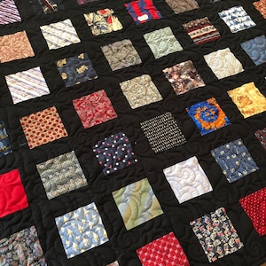 May include: A black quilt with a grid pattern of squares made from different patterned fabrics. The squares are all different colors and patterns, including stripes, polka dots, paisley, and floral prints.