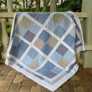 May include: A blue and white patchwork quilt with a quilted pattern. The quilt is made of different shades of blue and white fabric, and it has a white border.