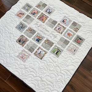 Könnte beinhalten: Eine weiße Steppdecke mit einem herzförmigen Design, das aus gerahmten Fotos und gemusterten Quadraten besteht. Die Steppdecke trägt den Schriftzug "The McKenna Family LOVE GROWS HERE". Die Ränder sind mit einem dunkelbraunen Rand versehen.