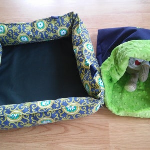 May include: Two pet beds, one is a square bed with a blue and green patterned fabric and a black center, the other is a round bed with a navy blue exterior and a green plush interior.
