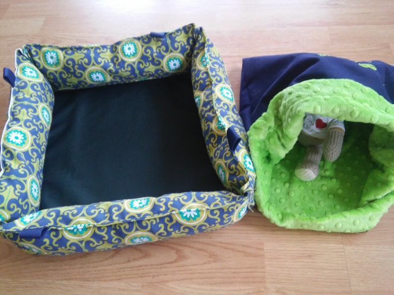 May include: Two pet beds, one is a square bed with a blue and green patterned fabric and a black center, the other is a round bed with a navy blue exterior and a green plush interior.