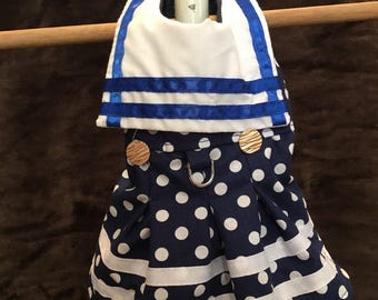 May include: A blue and white polka dot dress with white ribbon trim and blue ribbon accents. The dress has gold buttons and a silver D-ring.