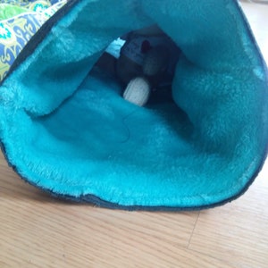 May include: A teal blue fabric-lined pouch with a stuffed animal inside. The pouch is made of a soft, fuzzy material.