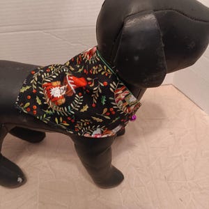 May include: A black dog mannequin wearing a Christmas-themed bandana with a red, green, and white pattern. The bandana features a small, cartoon-like Santa Claus figure and holly leaves.