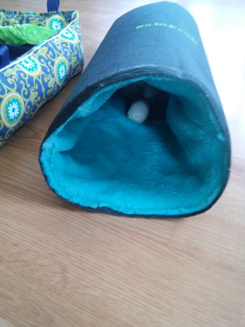 May include: A black and blue cat tunnel with a soft, blue, plush interior. A white ball is visible inside the tunnel.