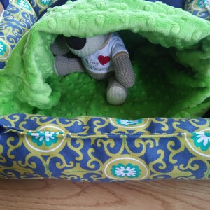 May include: A green and blue patterned pet bed with a plush green lining. A stuffed animal is inside the bed.