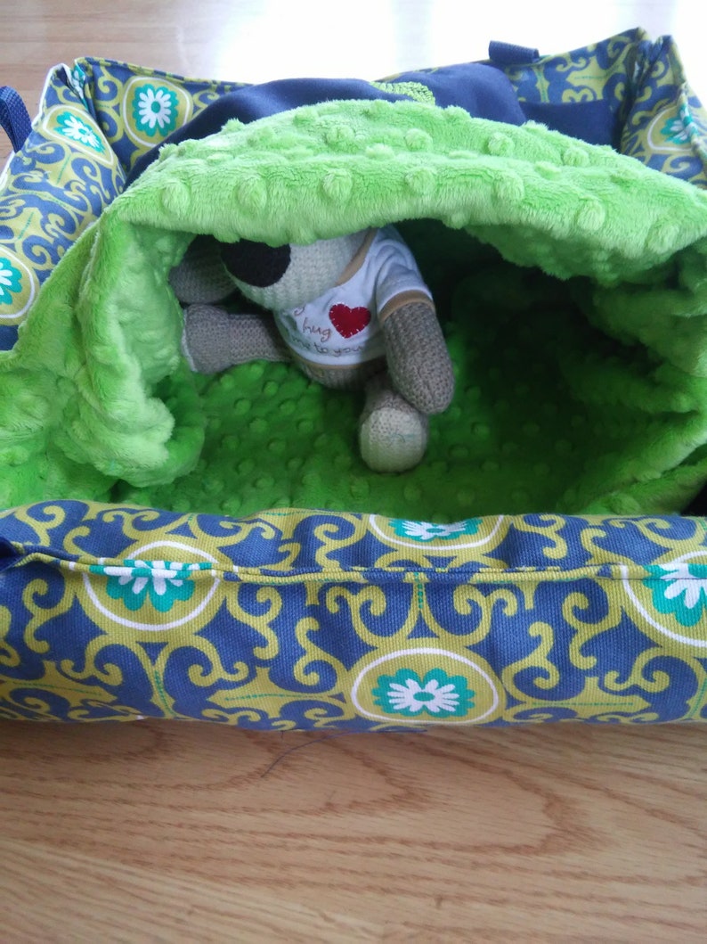 May include: A green and blue patterned pet bed with a plush green lining. A stuffed animal is inside the bed.