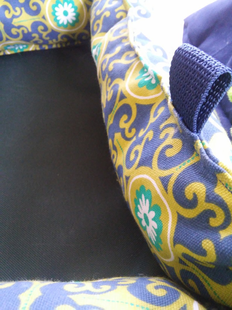 May include: A blue and yellow patterned fabric with a blue strap. The fabric has a floral design with white flowers.