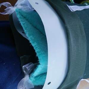 May include: A white plastic collar with a turquoise blue plush lining and white ribbon ties. The collar has holes on the sides.