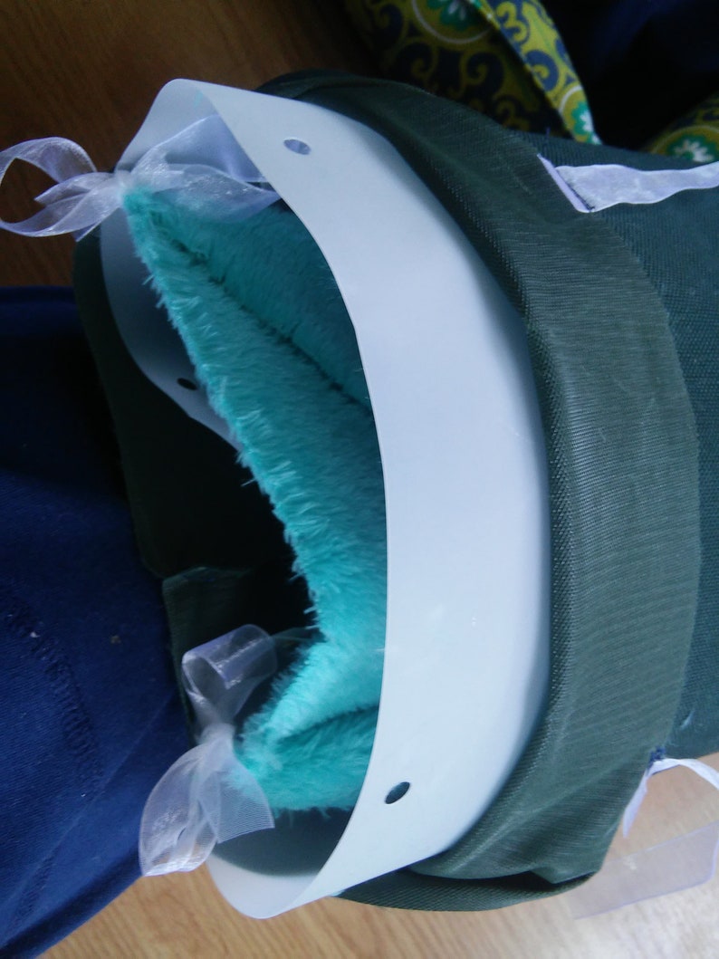 May include: A white plastic collar with a turquoise blue plush lining and white ribbon ties. The collar has holes on the sides.