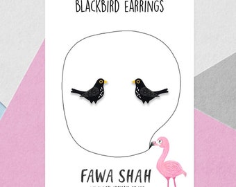Può includere: Orecchini a forma di merlo nero su una carta bianca con il testo "Blackbird Earrings" e "Fawa Shah" con un'illustrazione di fenicottero rosa.