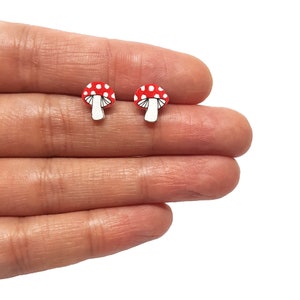 Può includere: Un paio di orecchini a bottone a forma di fungo rosso e bianco. I funghi hanno steli bianchi e cappelli rossi con pois bianchi.