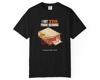 May include: A black t-shirt featuring a graphic of a worn book with the text I GOT TDS FROM READING, a red OVERDUE stamp, and a small label reading CONTAMINATED WITH FACTS. Below the book, the text reads It started with a book.