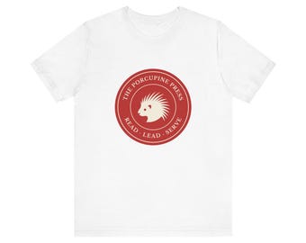 Könnte beinhalten: Ein weißes kurzärmeliges T-Shirt mit einem kreisförmigen roten Logo auf der Brust. Das Logo zeigt in der Mitte die Silhouette eines weißen Stachelschweins, umgeben von dem Text THE PORCUPINE PRESS und den Wörtern READ, LEAD, SERVE in Weiß.