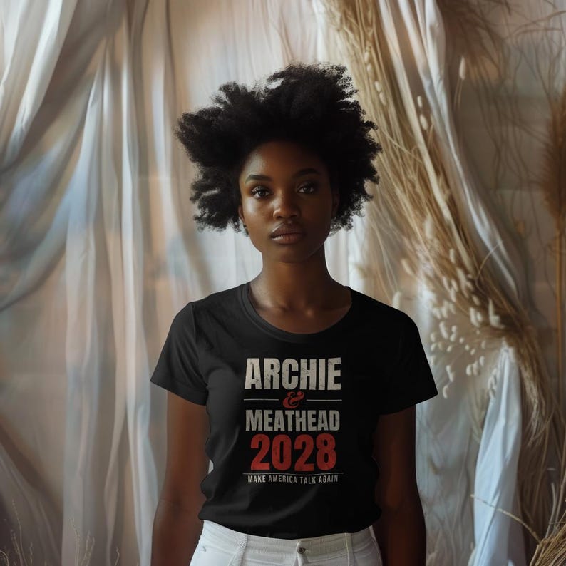 May include: A black short-sleeved t-shirt featuring the white and red text ARCHIE & MEATHEAD 2028 and the smaller text MAKE AMERICA TALK AGAIN printed on the front. The shirt has a crew neckline and a standard fit.