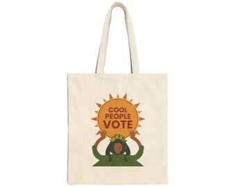 May include: A beige canvas tote bag featuring a graphic illustration of a person with dark hair adorned with flowers, holding up a large orange sun. The sun contains the text COOL PEOPLE VOTE in bold, dark brown, capitalized letters.