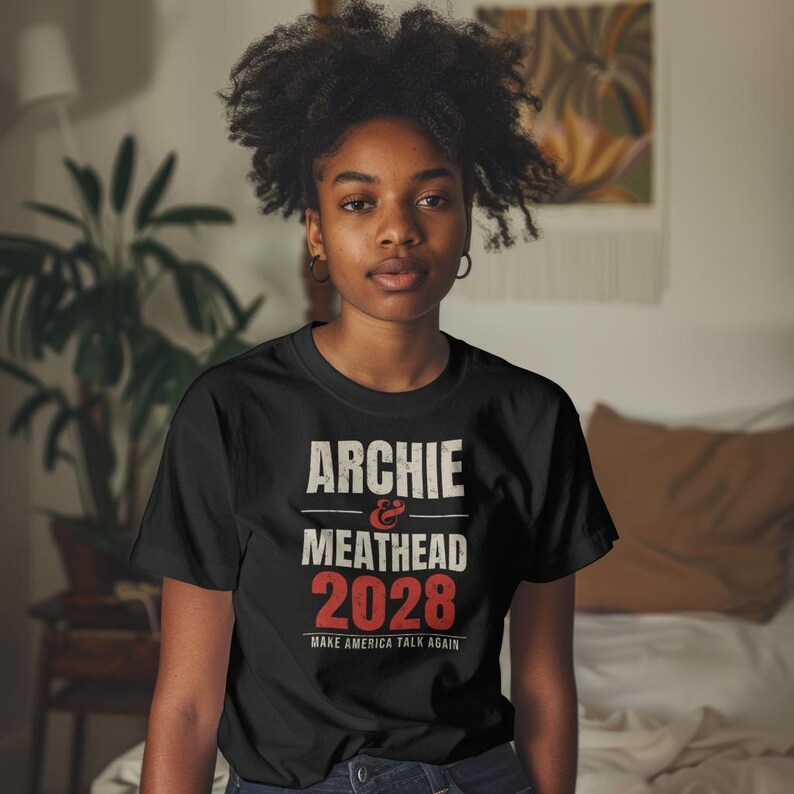 May include: A black short-sleeved t-shirt featuring white and red text that reads ARCHIE & MEATHEAD 2028 MAKE AMERICA TALK AGAIN. The design is centered on the chest with a distressed, vintage-style font and bold red numbers.