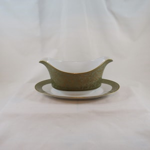 May include: A white gravy boat with a green and gold floral pattern and a matching saucer.