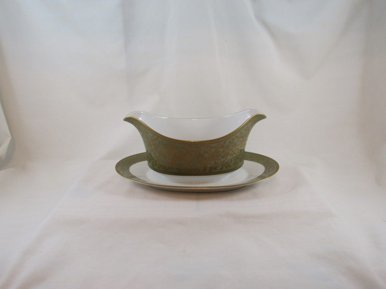 May include: A white gravy boat with a green and gold floral pattern and a matching saucer.