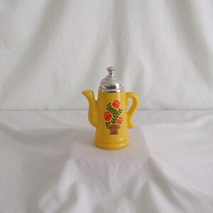 May include: Yellow ceramic teapot with a silver lid and a floral design. The teapot has a floral design with red and green flowers in a basket.