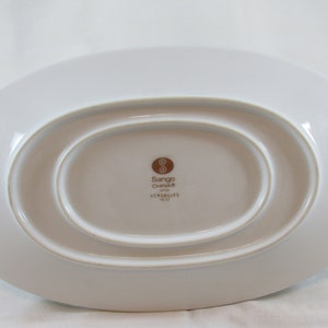 May include: A white oval-shaped serving dish with a raised rim. The bottom of the dish has a brown logo that reads "Sango China" and "Versailles 18-12".