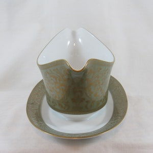 May include: A green and gold gravy boat with a matching saucer. The boat features a decorative floral pattern with gold accents.