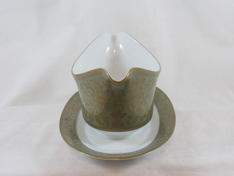 May include: A green and gold gravy boat with a matching saucer. The boat features a decorative floral pattern with gold accents.
