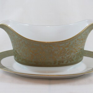 May include: A white porcelain gravy boat with a green and gold floral pattern. The boat has a matching saucer.