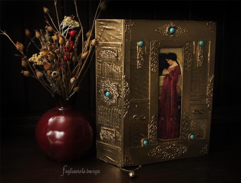 May include: A gold-colored book with intricate designs and turquoise gemstones. The book has a picture of a woman in a red dress on the front cover.