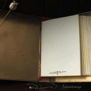 May include: An open, gold-colored journal with blank pages. The journal has a decorative design on the front cover and is closed with a gold clasp.