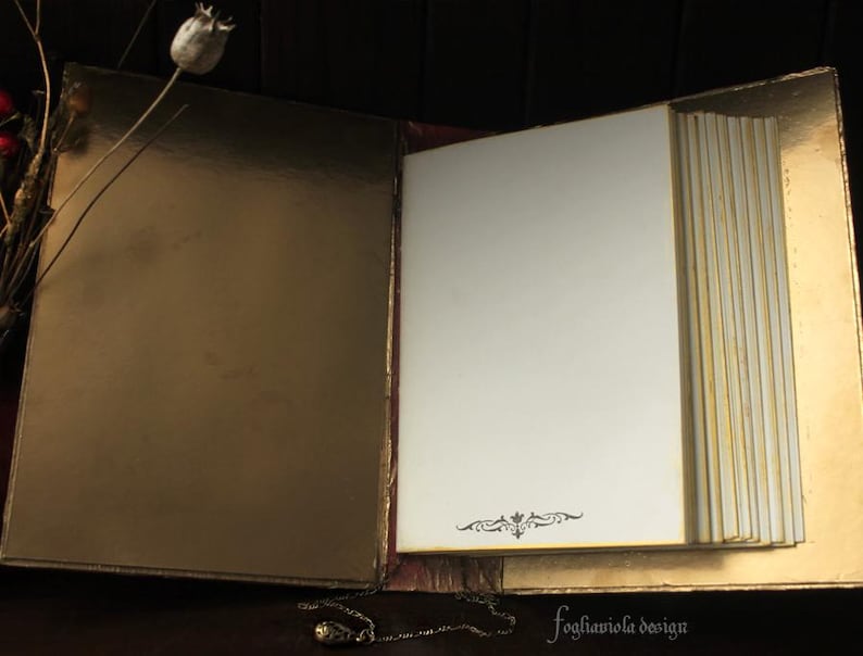 May include: An open, gold-colored journal with blank pages. The journal has a decorative design on the front cover and is closed with a gold clasp.