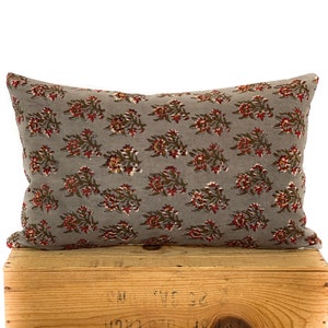 May include: A gray throw pillow with a floral pattern in shades of red and brown. The pillow is sitting on a wooden crate.