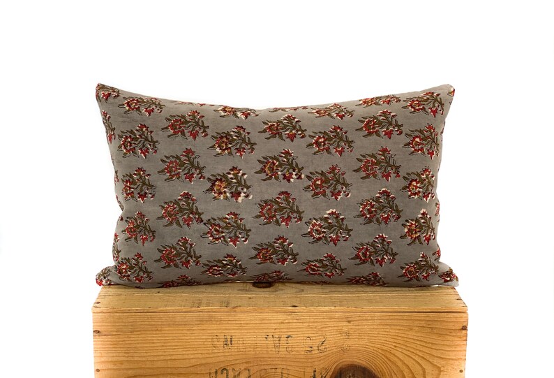 May include: A gray throw pillow with a floral pattern in shades of red and brown. The pillow is sitting on a wooden crate.