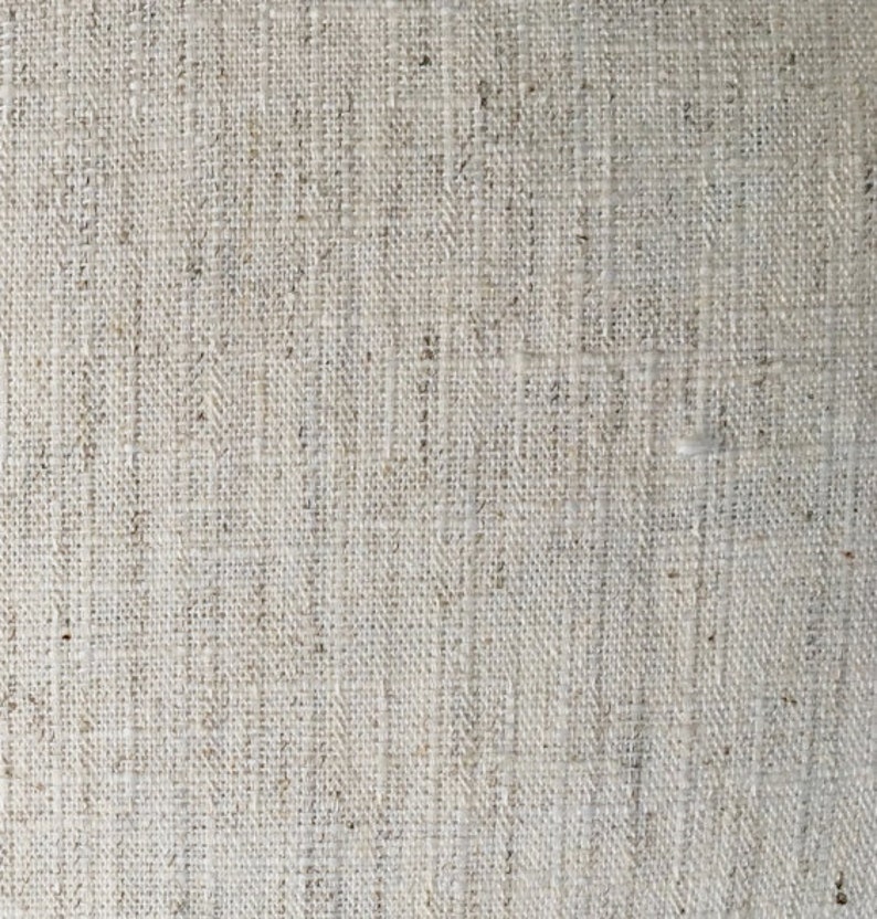 May include: Close-up of a natural woven fabric with a rough texture. The fabric is a light beige color and has a subtle pattern.