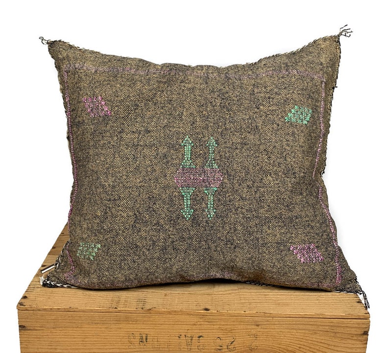 May include: A gray throw pillow with a pink and green geometric pattern. The pillow is made of a soft, woven fabric and has a fringed edge.