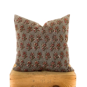 May include: A gray throw pillow with a red and green floral pattern. The pillow is sitting on a wooden crate.