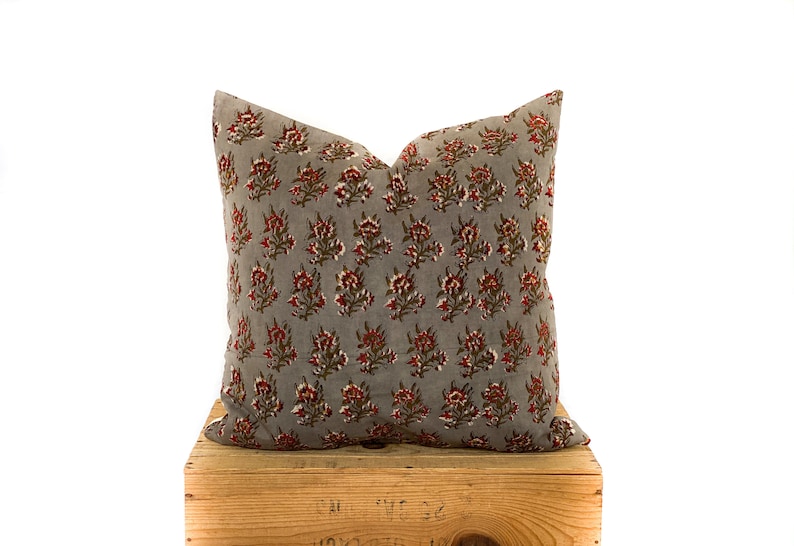 May include: A gray throw pillow with a red and green floral pattern. The pillow is sitting on a wooden crate.