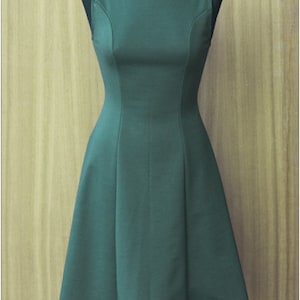 May include: A sleeveless, dark green dress with a fitted bodice and a flared skirt. The dress is on a mannequin against a woodgrain background.